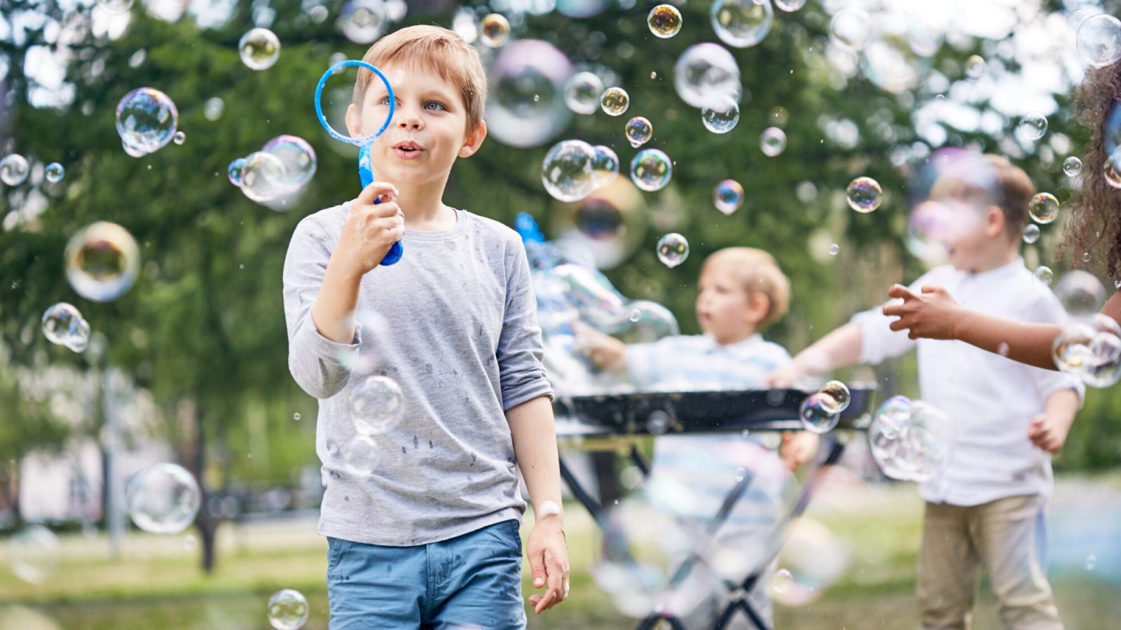 Group of little boys wrapped up in blowing colorful soap bubbles while gathered together at green public park
